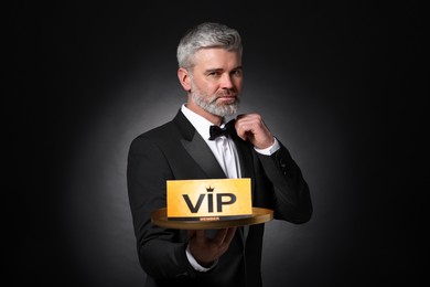 Handsome man holding tray with VIP sign on black background