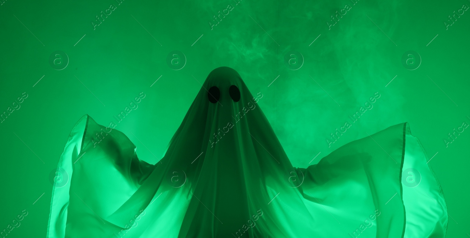 Photo of Creepy ghost. Woman covered with sheet in green light