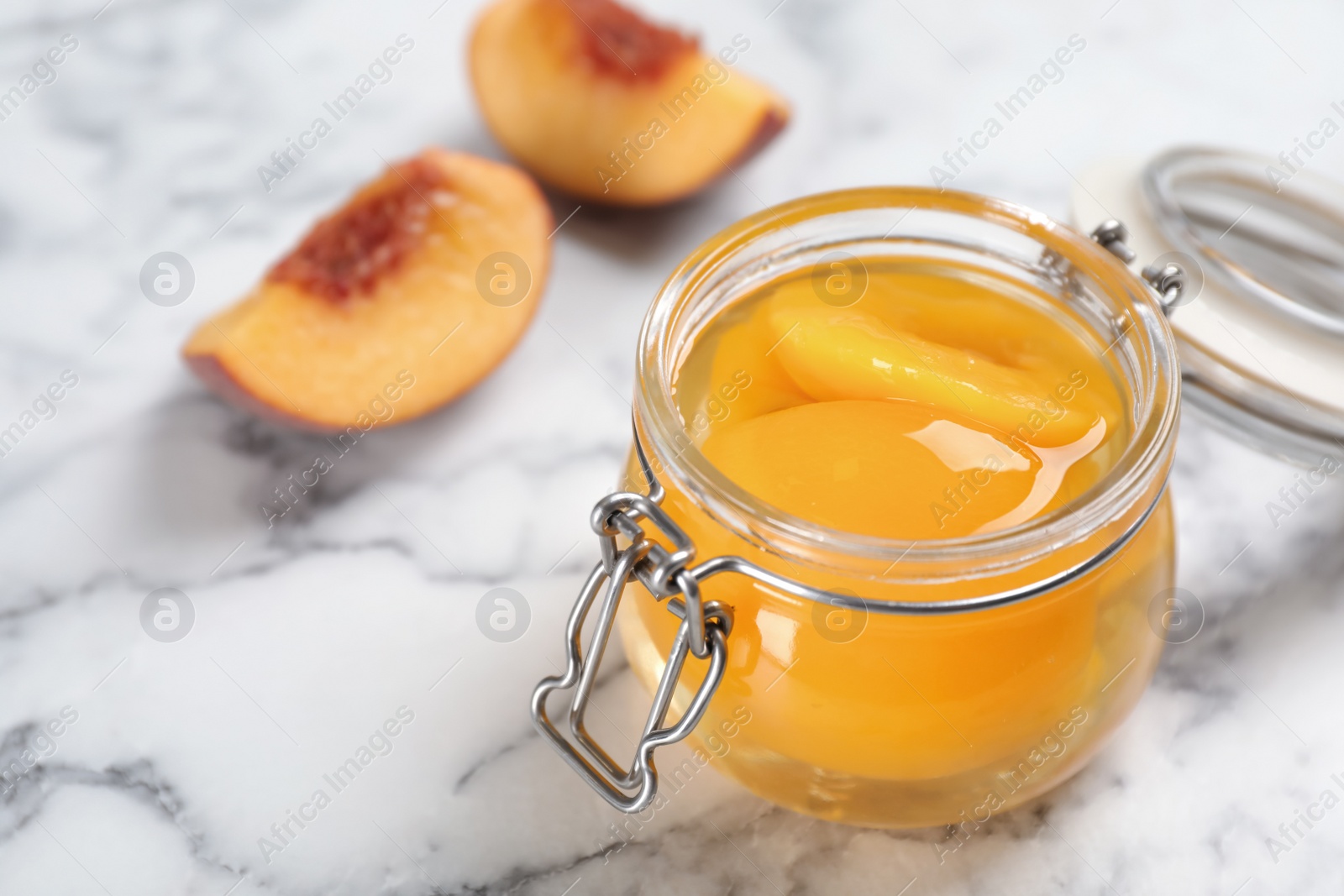 Photo of Glass jar with conserved peach halves on marble background. Space for text