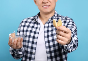 Photo of Happy man holding tasty fortune cookies with predictions on light blue background, closeup
