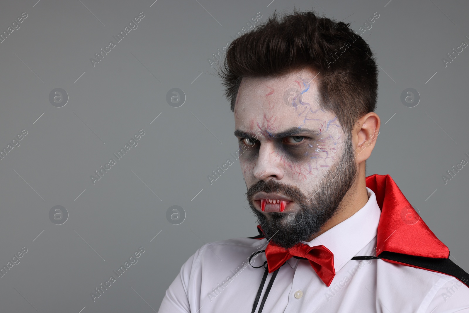 Photo of Man in scary vampire costume with fangs on light grey background, space for text. Halloween celebration