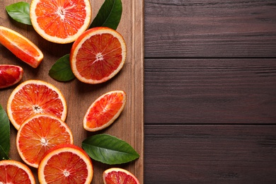 Photo of Slices of fresh ripe red oranges on wooden table, top view. Space for text