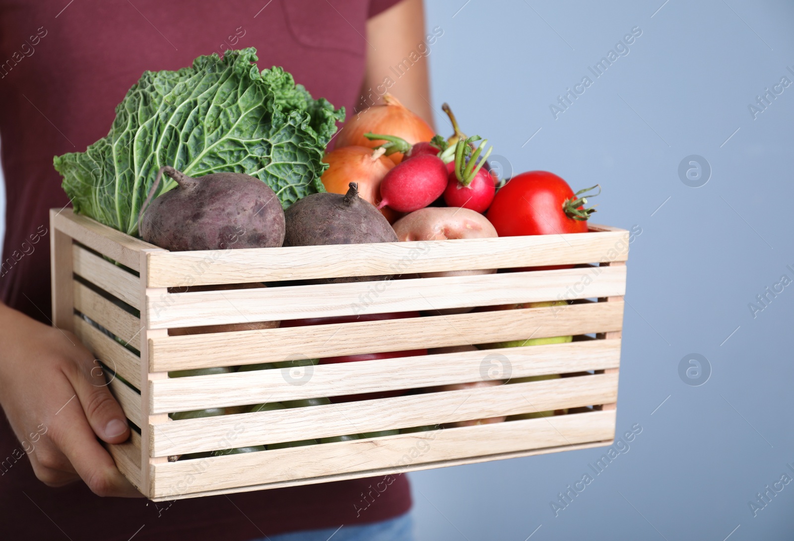 Photo of Farmer with wooden crate full of different vegetables and fruits on blue background, closeup. Harvesting time