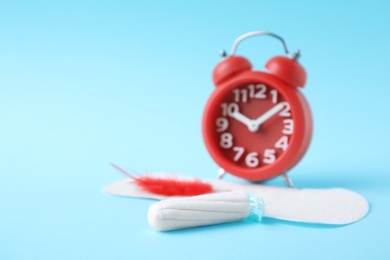 Photo of Different feminine hygiene products with red feather and alarm clock on color background, space for text. Gynecological care