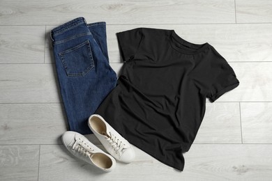 Photo of Stylish t-shirt, sneakers and jeans on white wooden background, flat lay