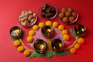 Happy Diwali. Composition with diya lamps, colorful rangoli, flowers and delicious Indian sweets on red table, above view