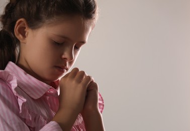 Photo of Cute little girl with hands clasped together praying on grey background. Space for text