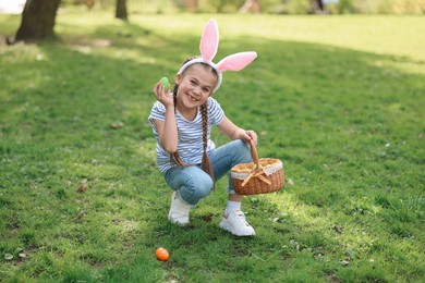 Photo of Easter celebration. Cute little girl in bunny ears hunting eggs outdoors