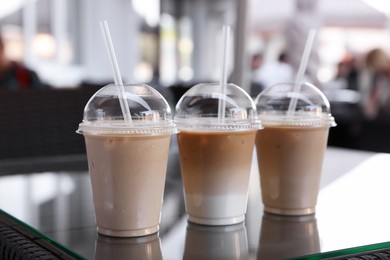 Photo of Plastic takeaway cups of delicious iced coffee on table in outdoor cafe