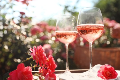Photo of Glasses of rose wine on table in blooming garden
