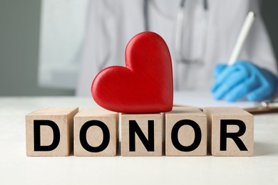 Photo of Wooden cubes with word Donor and decorative heart on white table