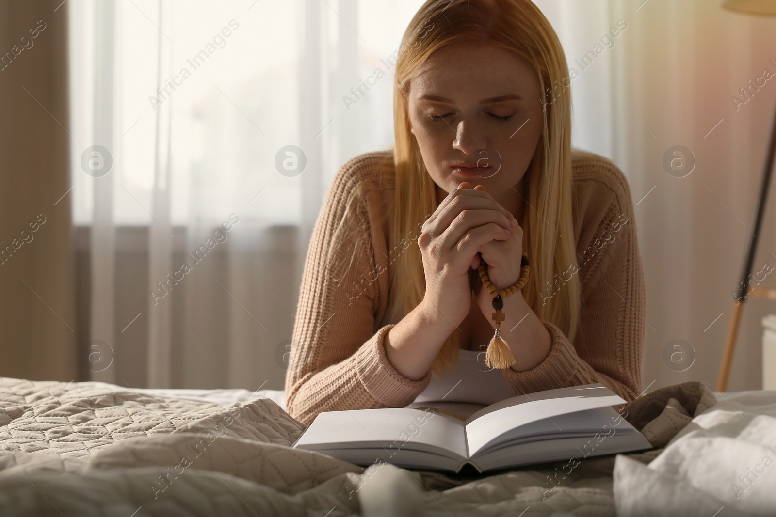 Photo of Religious young woman praying over Bible in bedroom