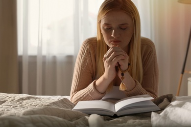 Photo of Religious young woman praying over Bible in bedroom