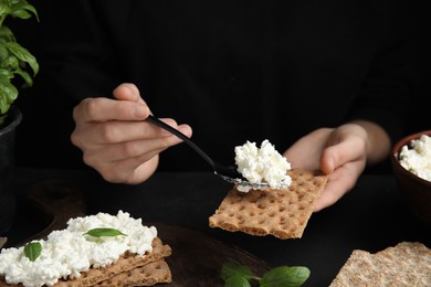 Photo of Woman spreading cottage cheese onto crispy cracker at black table, closeup