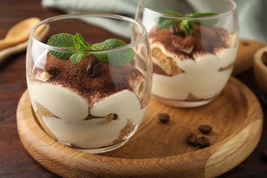 Photo of Delicious tiramisu in glasses, mint leaves and coffee beans on wooden table, closeup