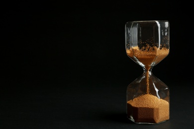 Photo of Hourglass with golden sand on black background. Space for text