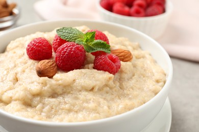 Photo of Tasty oatmeal porridge with raspberries and almond nuts in bowl on table, closeup