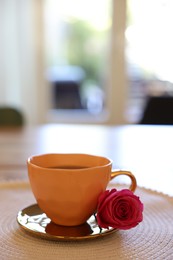 Photo of Cup of hot drink and red rose on table indoors. Space for text