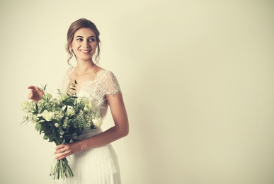 Photo of Young bride wearing wedding dress with beautiful bouquet on beige background. Space for text