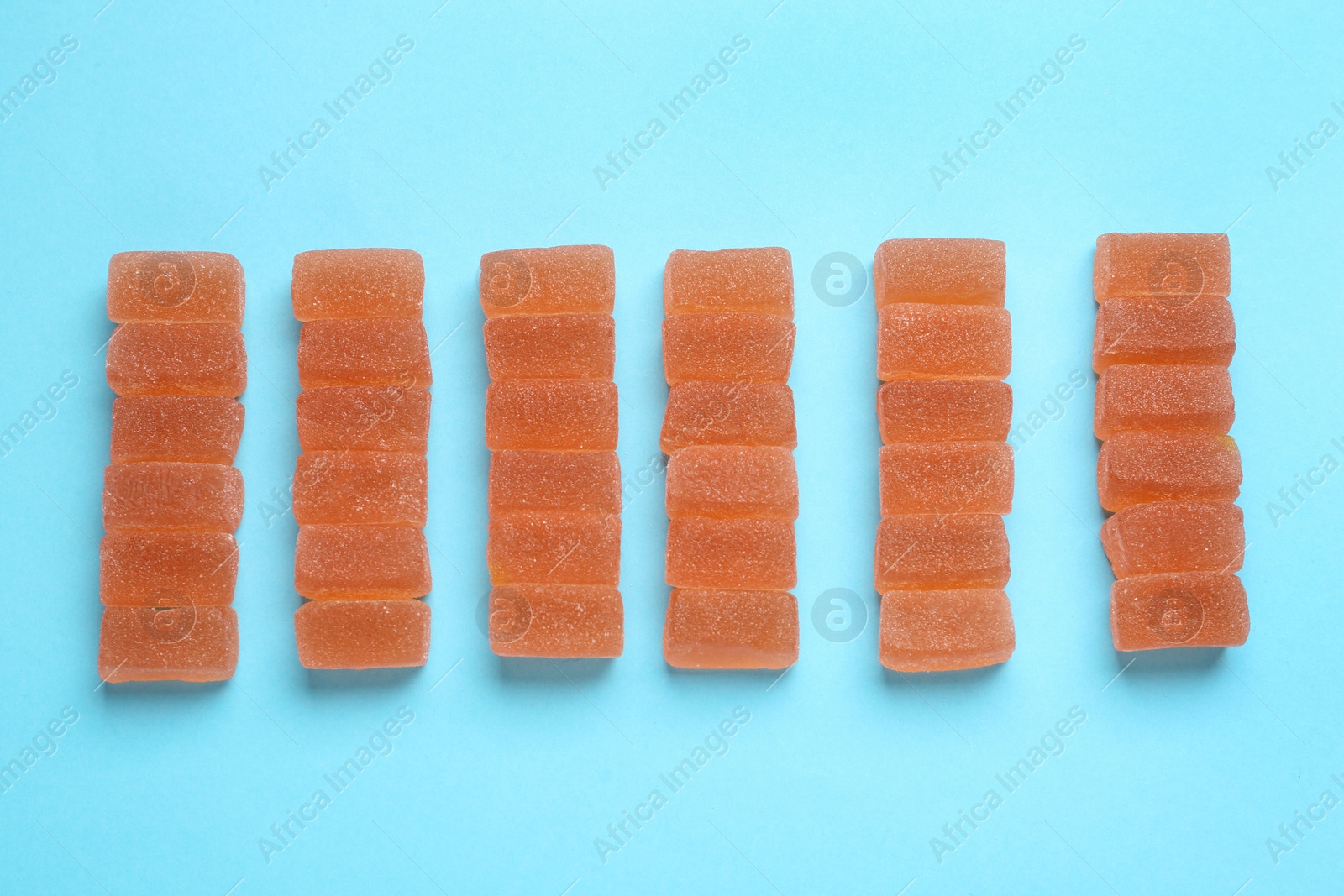 Photo of Tasty orange jelly candies on light blue background, flat lay