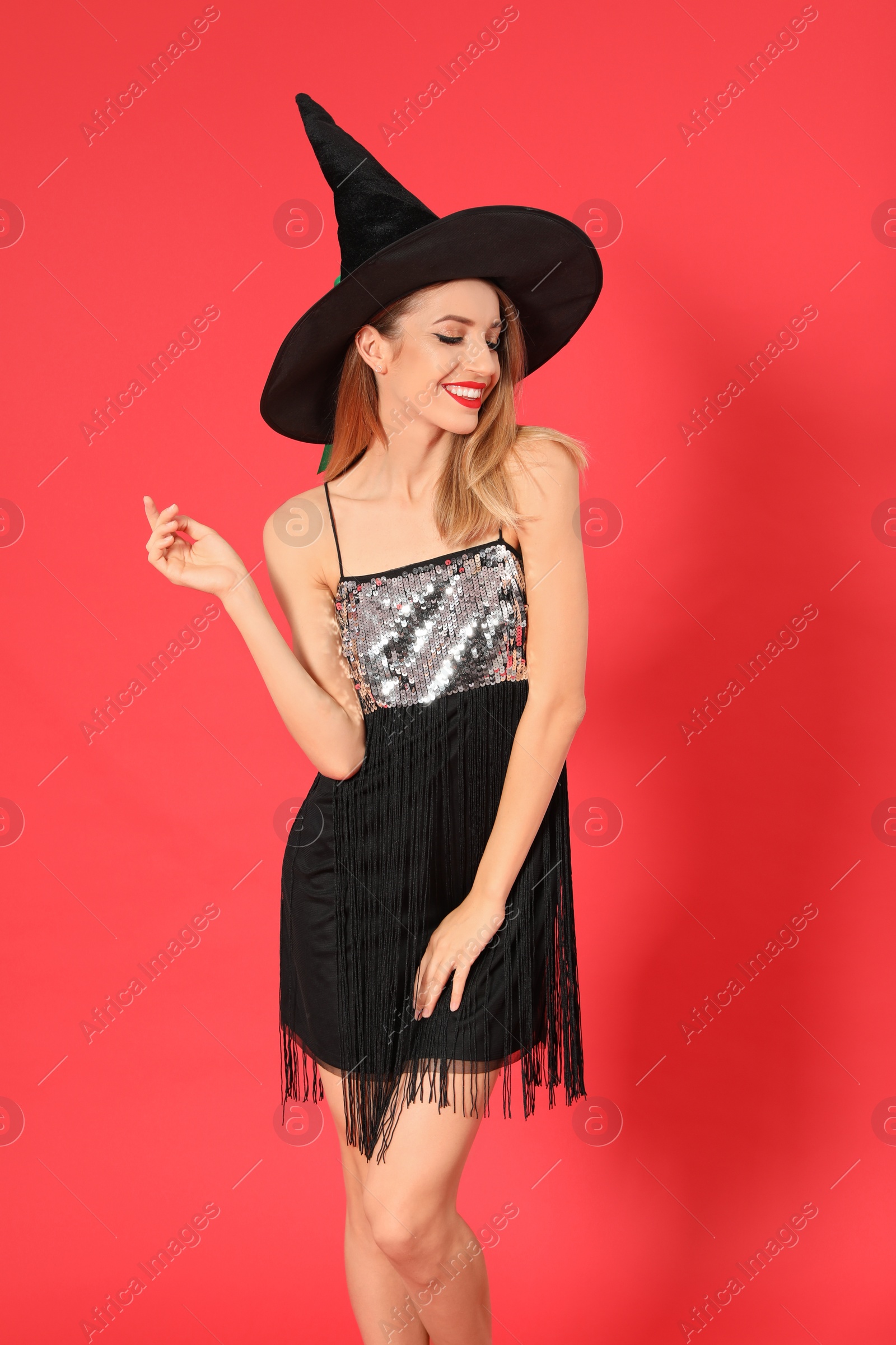 Photo of Beautiful young woman wearing witch costume for Halloween party on red background