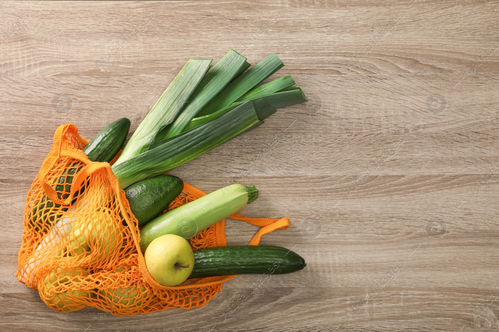 Photo of Net bag with vegetables and fruits on wooden table, top view. Space for text