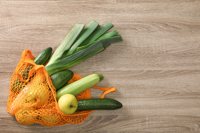 Net bag with vegetables and fruits on wooden table, top view. Space for text