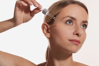 Beautiful woman applying cosmetic serum onto her face on white background, closeup