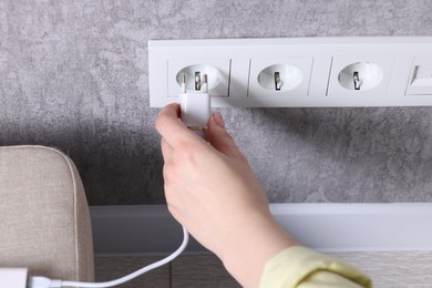 Woman plugging power bank into socket on grey wall indoors, closeup