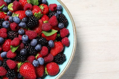 Photo of Many different fresh ripe berries in bowl on white wooden table, top view. Space for text