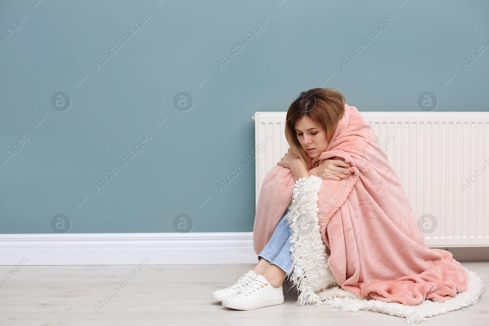 Photo of Sad woman suffering from cold on floor near radiator