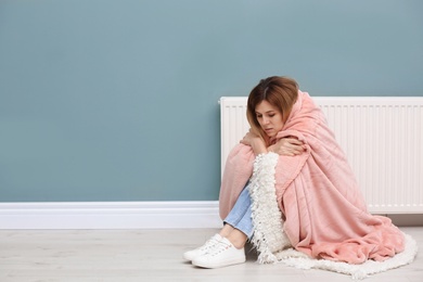 Sad woman suffering from cold on floor near radiator