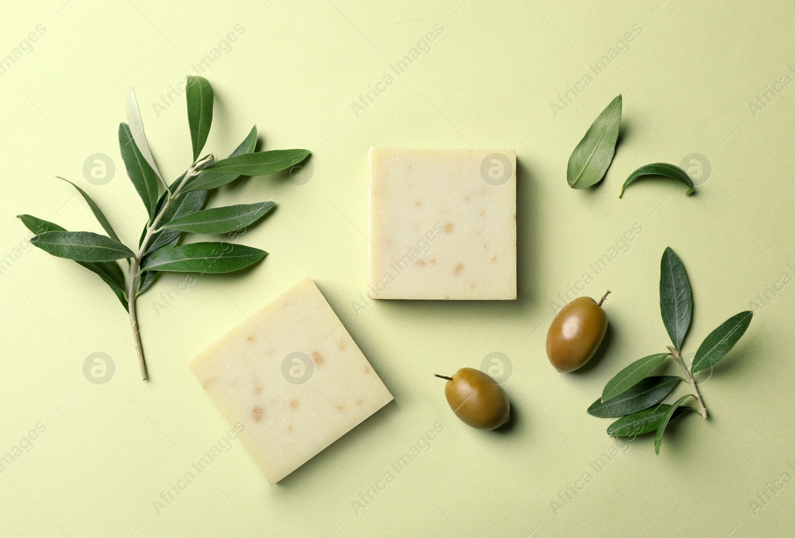 Photo of Handmade soap bars and leaves with olives on color background, top view