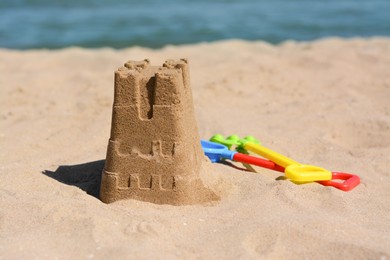 Photo of Sand castle and child plastic toys on beach near sea. Space for text