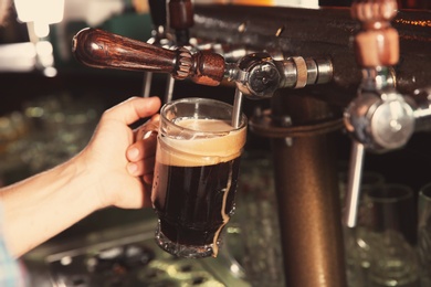 Photo of Bartender pouring beer from tap into glass in bar, closeup