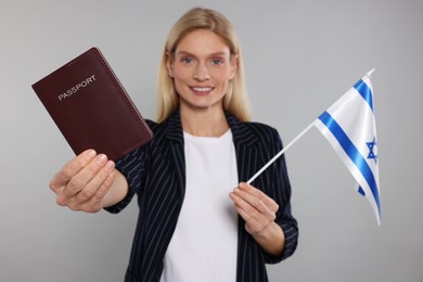 Photo of Immigration. Happy woman with passport and flag of Israel on gray background, selective focus