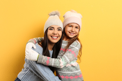 Photo of Happy mother and daughter in warm clothes on yellow background. Winter vacation