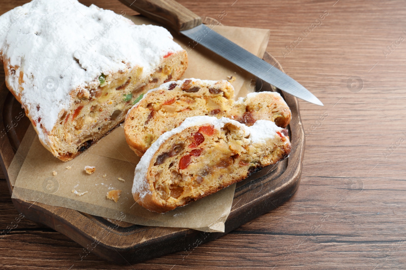 Photo of Traditional Christmas Stollen with icing sugar on wooden table, space for text