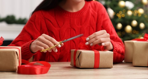 Photo of Woman decorating Christmas gift box at wooden table indoors, closeup