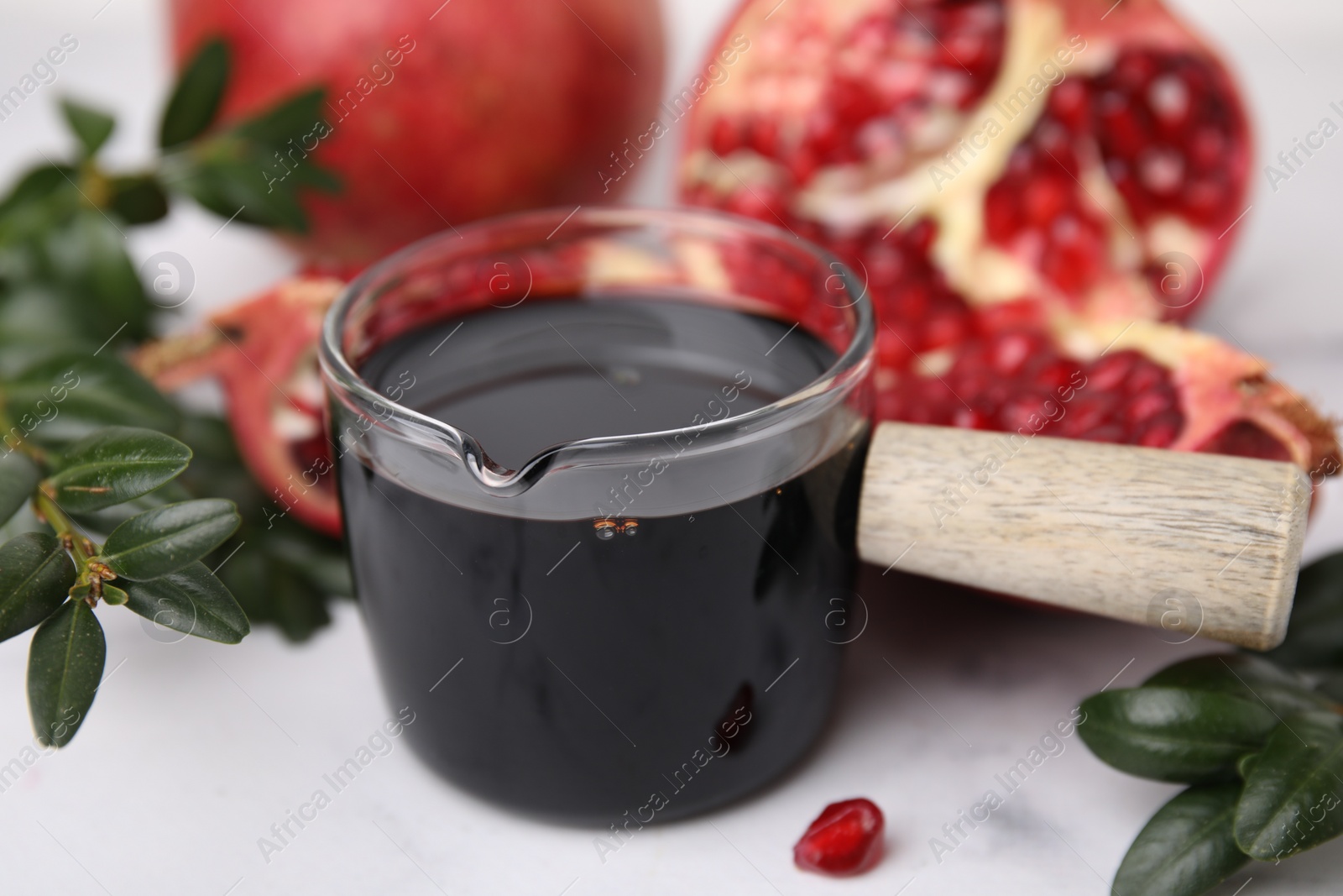 Photo of Tasty pomegranate sauce, fruits and branches on white table, closeup