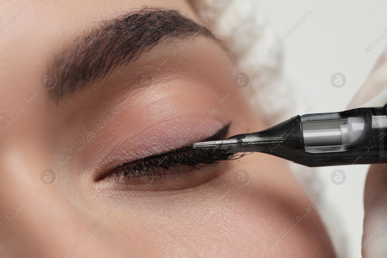 Photo of Young woman undergoing procedure of permanent eye makeup, closeup