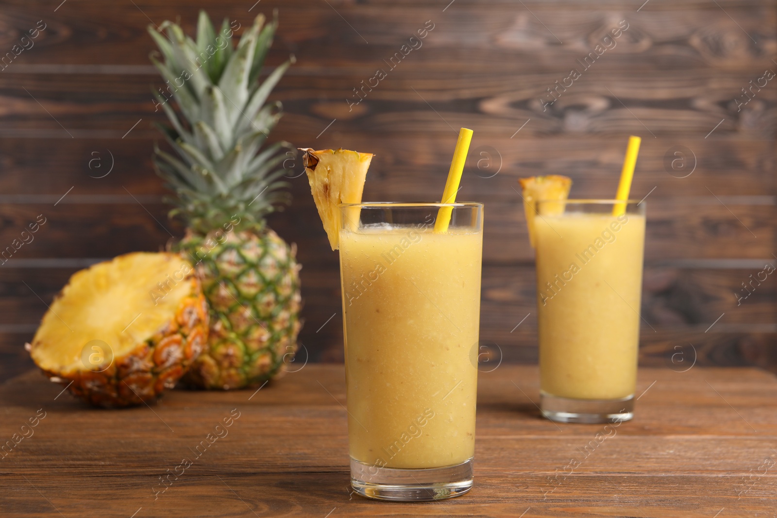Photo of Tasty pineapple smoothie, whole and cut fruit on wooden table