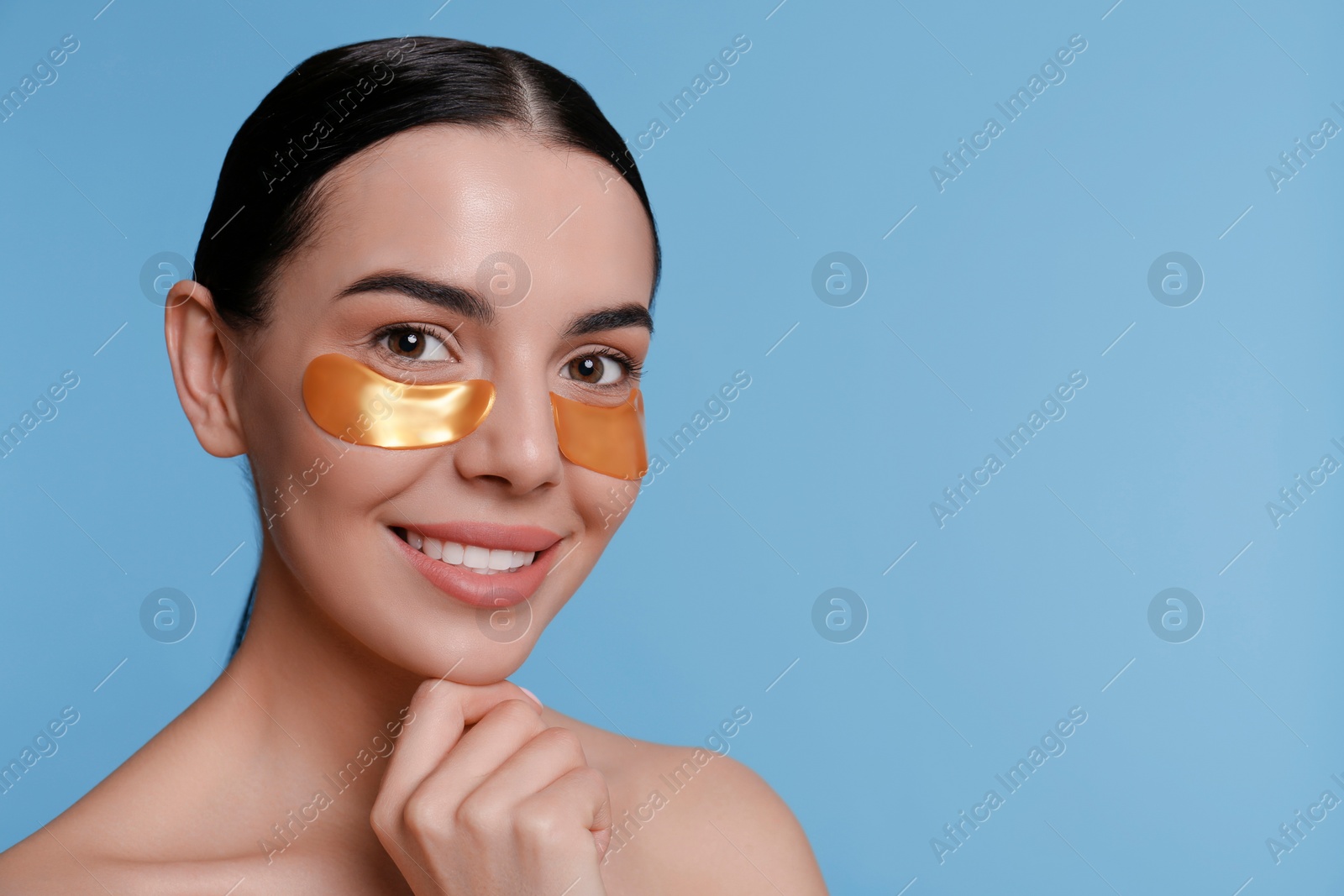Photo of Beautiful young woman with under eye patches on light blue background, space for text