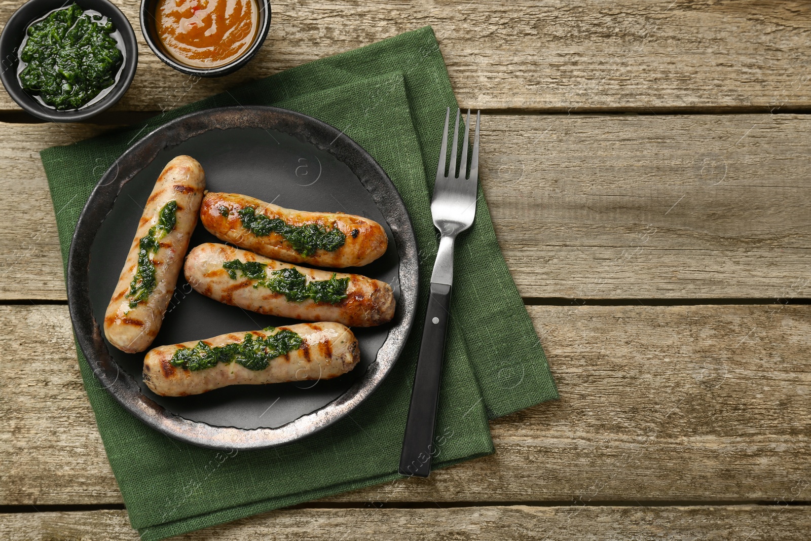 Photo of Tasty fresh grilled sausages served with sauces on wooden table, flat lay. Space for text