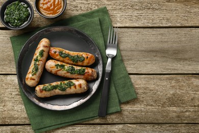 Photo of Tasty fresh grilled sausages served with sauces on wooden table, flat lay. Space for text