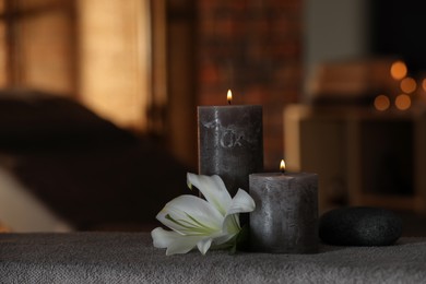 Photo of Spa composition with burning candles, lily flower and stone on massage table in wellness center, space for text