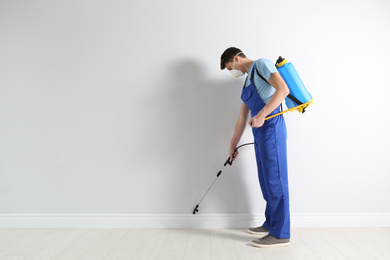 Pest control worker spraying pesticide in room. Space for text