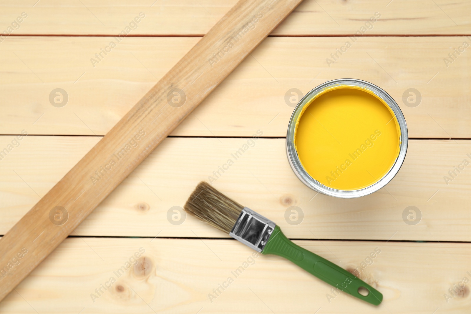 Photo of Can of yellow paint and brush on wooden table, flat lay. Space for text