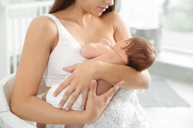Photo of Young woman breastfeeding her baby in nursery, closeup