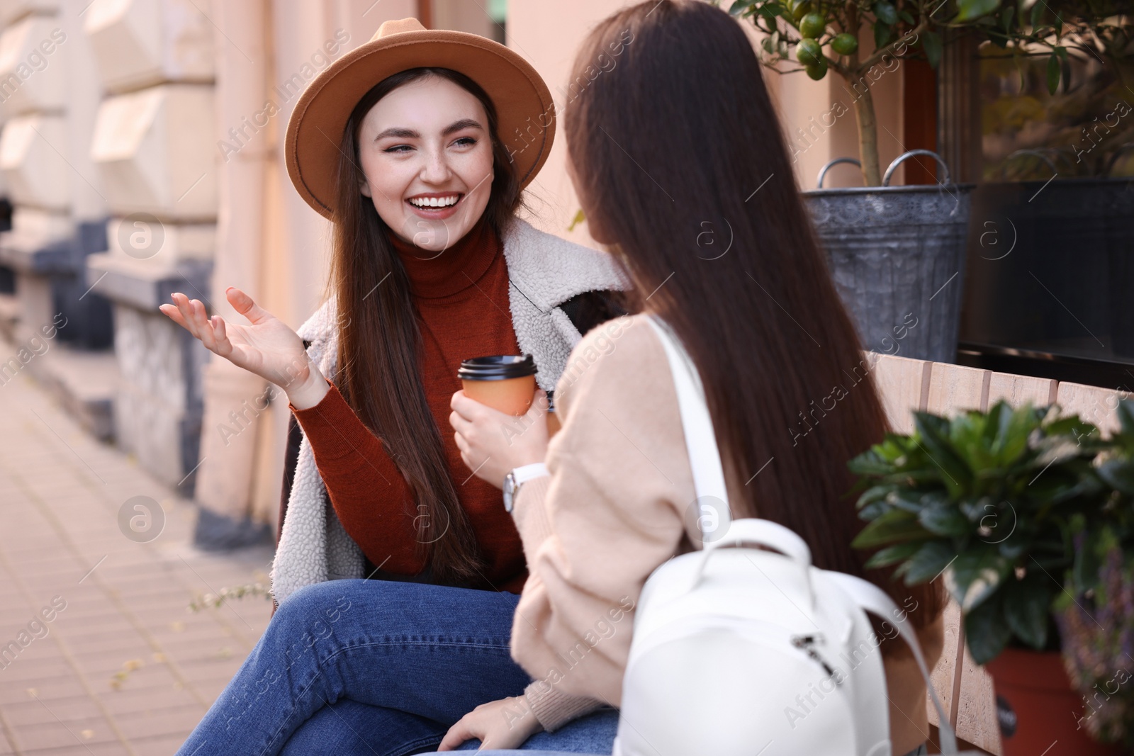 Photo of Happy friends with paper cups of coffee talking outdoors